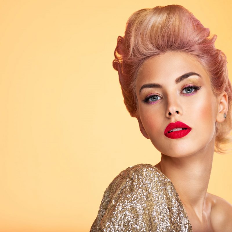 Beautiful woman with creative hairstyle, vivid makeup. Fashionable girl. Beautiful young woman with red lips. Stunning blonde girl. Bright eye makeup. Attractive caucasian model in golden jacket.